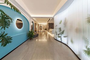 A hallway with a curved ceiling, a blue accent wall with a circular cutout, and a plant. - Allston Hotel (Xiamen)