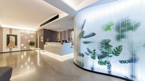 A modern reception area with a curved glass wall featuring a tropical leaf design. - Allston Hotel (Xiamen)