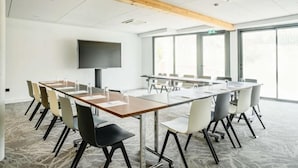 A conference room with a long table, chairs, a flat-screen TV, and large windows.