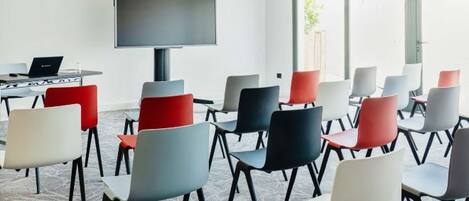 A conference room with a large flat-screen TV, multiple chairs, and a table with a laptop.