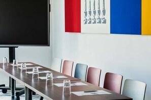 Una sala de conferencias con una larga mesa, sillas y una pantalla para proyector.