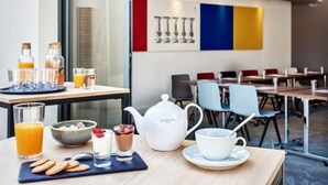 A breakfast setup with a teapot, cups, glasses, and a bowl of cereal on a table.