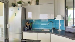 Et moderne køkken med køleskab, vask og bordplade. Der er plantede planter på bordpladen og et vindue med udsigt.