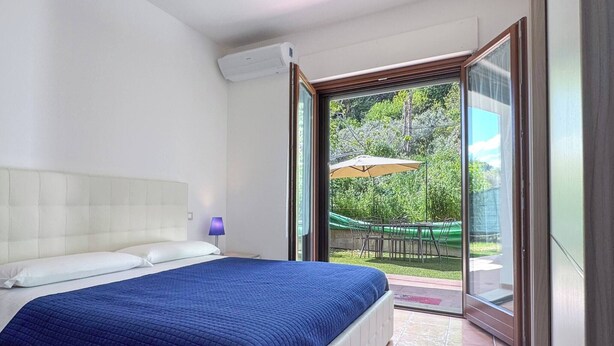 Ein Schlafzimmer mit Bett, Fenster und Blick ins Freie.