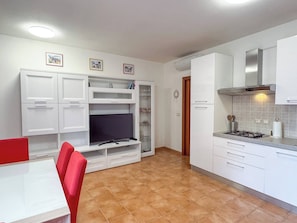 A compact kitchen with white cabinets, a built-in TV, and a dining area with a red chair.