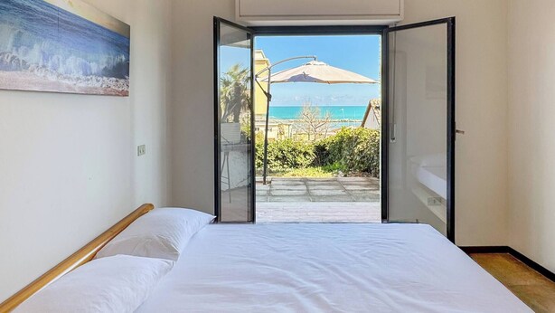 A bedroom with a bed, a painting on the wall, and a view of the sea through an open door.