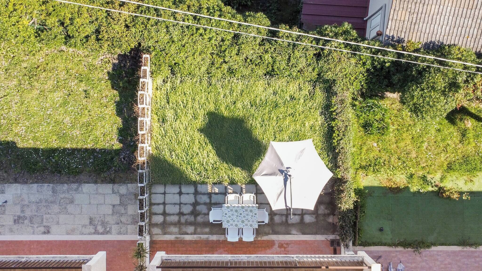 Vista aérea de una terraza en la azotea con una mesa y sillas, rodeada de vegetación y un muro de ladrillo.