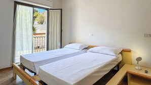A room with two beds, a small bedside table with a lamp, and a window with curtains.