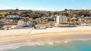 A coastal hotel with multiple buildings, a beach, and a mountainous backdrop.