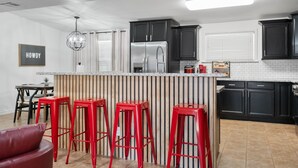 A modern kitchen with dark cabinets, a stainless steel refrigerator, and a bar area with red stools. - Ultimate Tech Home - Ready for Football Season! (Lubbock)