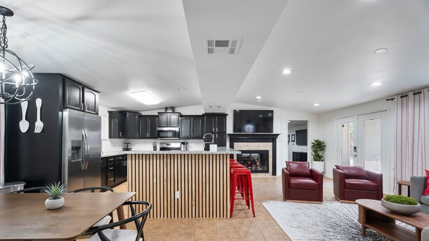 A modern kitchen with dark cabinets, a stainless steel refrigerator, and a wooden island with red bar stools. - Ultimate Tech Home - Ready for Football Season! (Lubbock)
