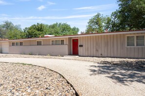 Un motel d’un seul étage, avec une porte rouge, une allée en gravier et un petit espace de stationnement.