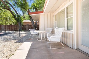 Une terrasse avec une table et quatre chaises, une clôture en bois et des arbres en arrière-plan.