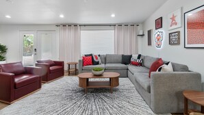 A modern living room with a grey sofa, red and black cushions, a wooden coffee table, and a patterned rug. - Ultimate Tech Home - Ready for Football Season! (Lubbock)