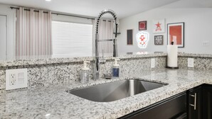 A kitchen with a granite countertop, stainless steel sink, and modern faucet. There are two soap dispensers and a white vase on the counter. - Ultimate Tech Home - Ready for Football Season! (Lubbock)