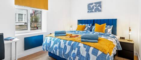 A bedroom with a bed, a nightstand, a desk, and a window with blinds.