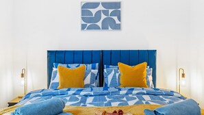 A bed with blue and white striped bedding, two yellow pillows, and a framed abstract artwork above it. - 5 Guests - 2 Bedrooms - Brighton Centre - Petsok (Brighton)