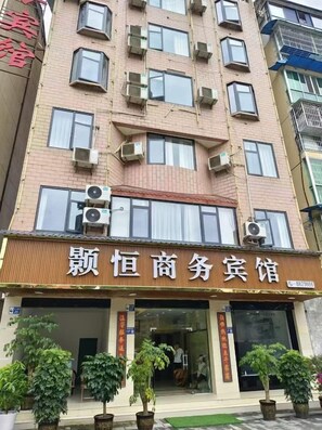 A multi-story building with a commercial space on the ground floor, featuring a storefront with signage and potted plants in front. - Pingwu Shuheng Business Hotel (Pingwu)
