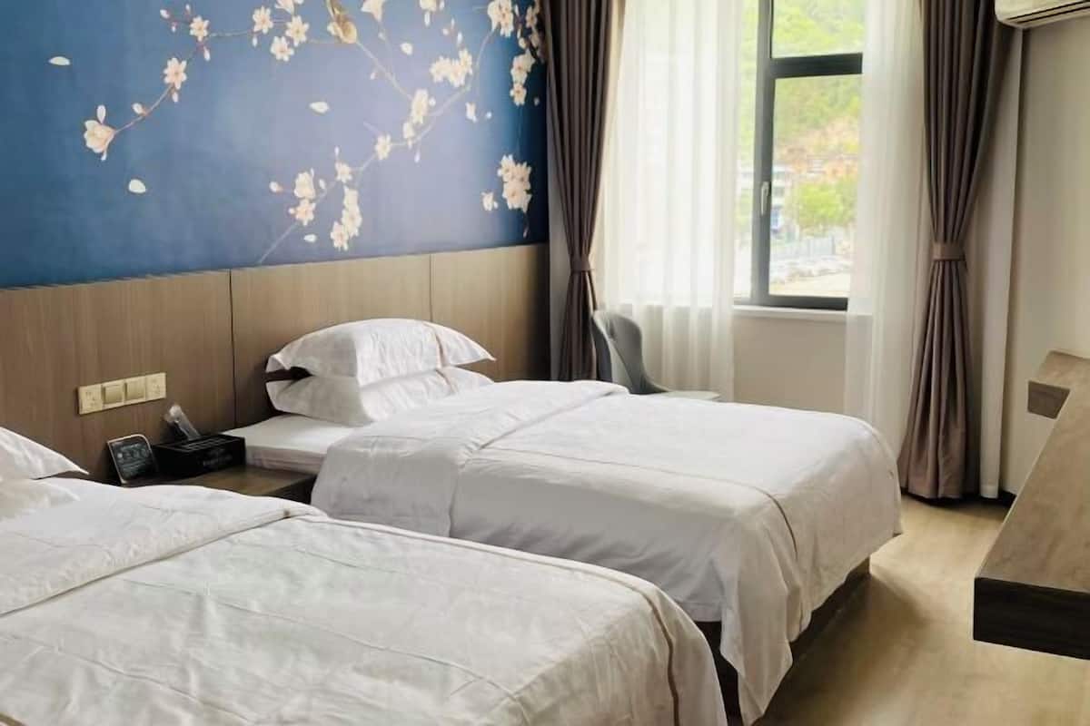 Een hotelkamer met twee bedden, een houten hoofdeinde, een muur met een bloemmotief en een raam met gordijnen.
