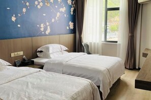Une chambre d’hôtel avec deux lits, une tête de lit en bois, un mur orné d’une fresque florale et une fenêtre avec des rideaux.