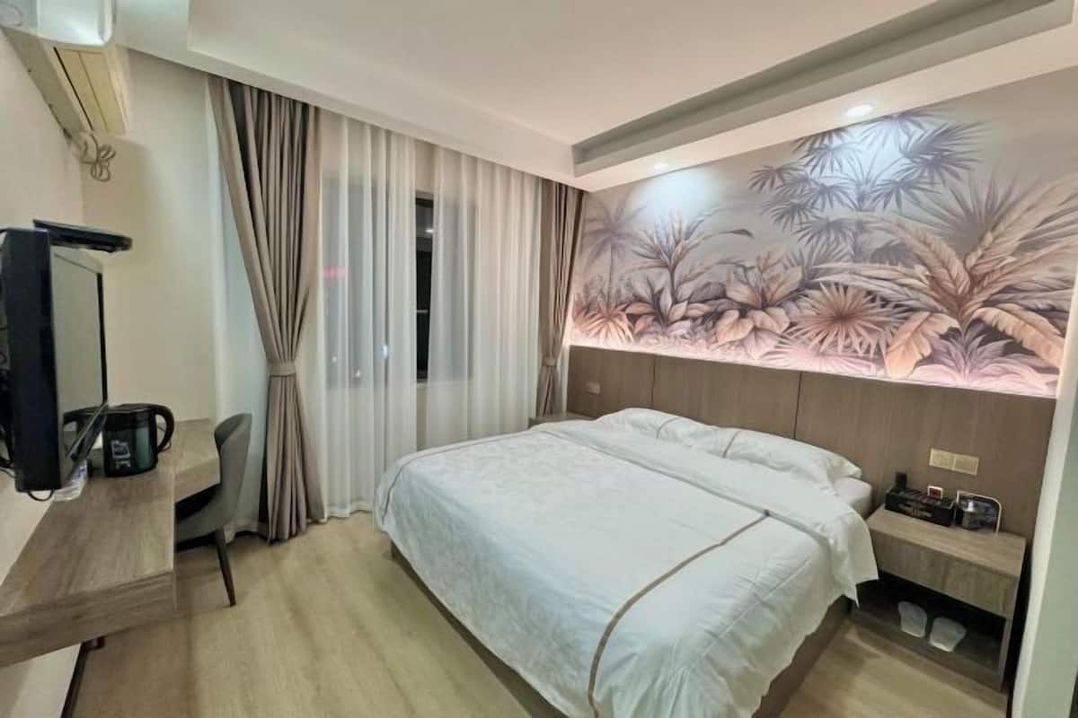 Een hotelkamer met een bed, een bureau met waterkoker, een spiegel en een muur met bladmotief.