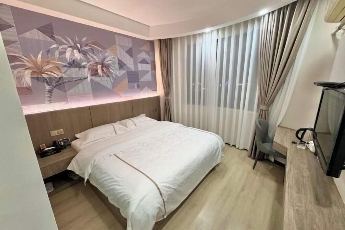 Een hotelkamer met een bed, een nachtkastje, een televisie en een muur met een geometrisch schilderij.