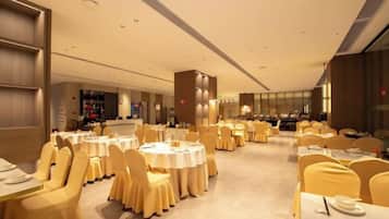 A banquet hall with round tables, yellow chairs, and a central pillar.