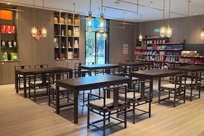 L’intérieur d’un restaurant, avec de nombreuses tables et chaises, des étagères remplies de divers objets et des luminaires suspendus.