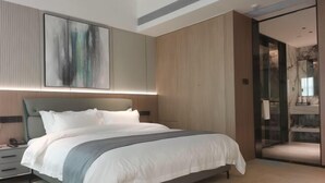 Une chambre moderne avec un grand lit, des tables de chevet, un tableau abstrait accroché au mur et une porte en verre donnant sur une salle de bain.