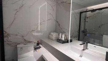 A modern bathroom with a marble wall, a toilet, a sink with a mirror, and a shower area.