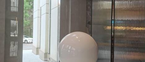 A modern interior with a spherical object on a reflective surface, a glass partition, and a view of the outdoors.