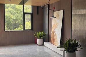 A room with a large window, a painting on the wall, and two potted plants. - Danxia Mountain Jincheng Hotel (Renhua)