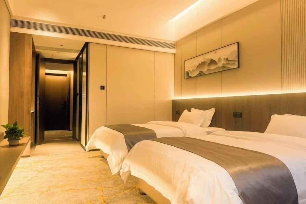 Hotellihuone, jossa on kaksi sänkyä, moderni sisustus, taulu seinällä ja käytävä, joka johtaa toiseen huoneeseen.