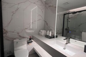 Un baño moderno con pared de mármol, un espejo grande, un inodoro y una zona de ducha.