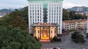 Un hôtel moderne doté d’une entrée imposante, entouré d’une végétation luxuriante et comprenant un espace de stationnement.