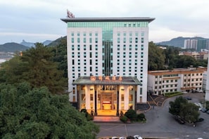 Un hôtel à plusieurs étages, doté d’une entrée principale, entouré de verdure et de zones de stationnement.