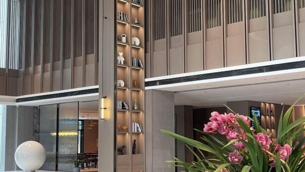 Un hall d’hôtel moderne avec une colonne centrale, un comptoir d’accueil et une grande plante en pot.