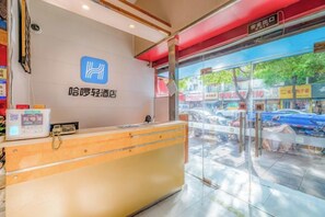A hotel reception desk with a logo, a digital check-in machine, and a view of the street outside.