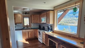 A kitchen with wooden cabinets, a built-in oven, and a window with a view of a lake and forest. - Mountain Cabin in Palmer, Ak (Palmer)