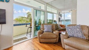 A spacious living area with a large sliding glass door leading to a balcony, a brown leather sofa, a matching armchair, and a patterned throw pillow. - BAYFRONT! AUGUST 8-10 OPEN FANTASTIC VIEWS & LOCATION WALK TO FOOD, SHOPS, OCEAN (San Diego)
