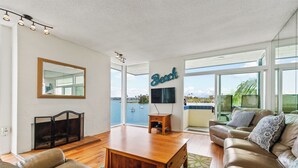 A spacious living room with a large window, a fireplace, a sofa, and a television. - BAYFRONT! AUGUST 8-10 OPEN FANTASTIC VIEWS & LOCATION WALK TO FOOD, SHOPS, OCEAN (San Diego)