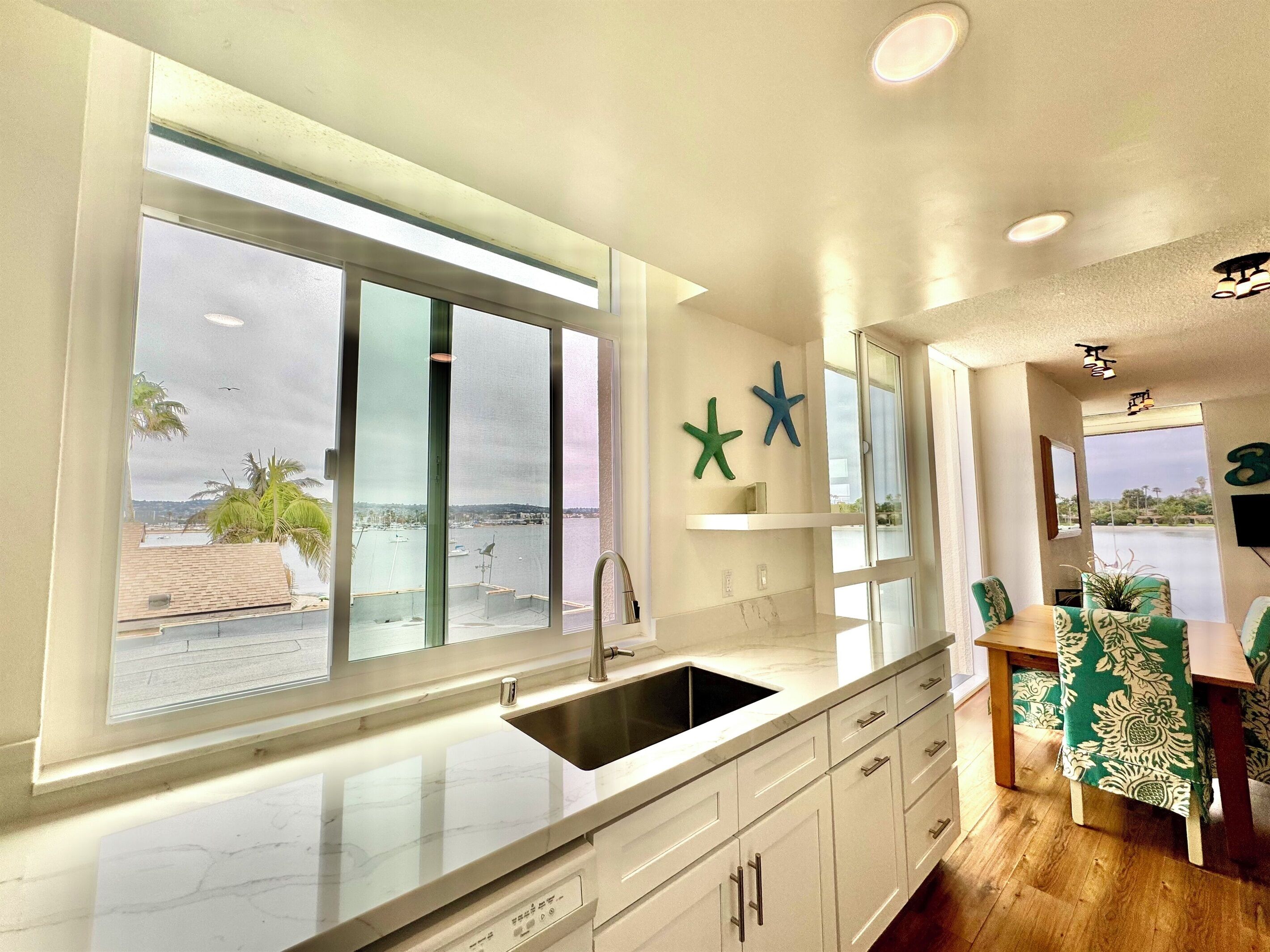 A modern kitchen with a large window, a sink, and a dining area with chairs.