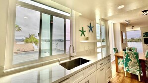 A modern kitchen with a large window, a sink, and a dining area with chairs. - BAYFRONT! AUGUST 8-10 OPEN FANTASTIC VIEWS & LOCATION WALK TO FOOD, SHOPS, OCEAN (San Diego)