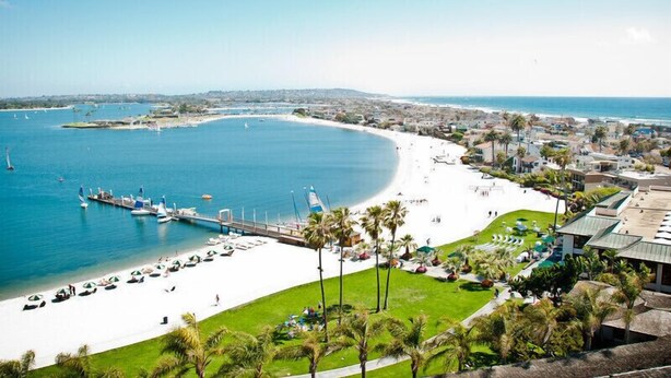 A coastal resort with a white sandy beach, a marina with boats, and a backdrop of a clear blue sea and distant hills. - BAYFRONT! AUGUST 8-10 OPEN FANTASTIC VIEWS & LOCATION WALK TO FOOD, SHOPS, OCEAN (San Diego)