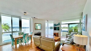 A spacious living room with a large window overlooking a body of water, a sofa, a dining area with chairs, and a TV mounted on the wall. - BAYFRONT! AUGUST 8-10 OPEN FANTASTIC VIEWS & LOCATION WALK TO FOOD, SHOPS, OCEAN (San Diego)