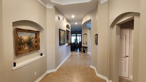 A hallway with arched doorways, framed artwork on the walls, and a tiled floor. - Luxury 4BR Cypress Home + Office Theater + Huge Fenced Yard + Pet Friendly (Cypress)