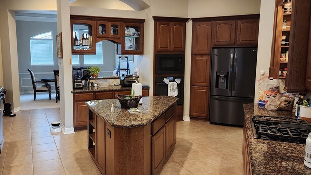 A kitchen with granite countertops, wooden cabinets, a central island, a refrigerator, and a stove. - Luxury 4BR Cypress Home + Office Theater + Huge Fenced Yard + Pet Friendly (Cypress)