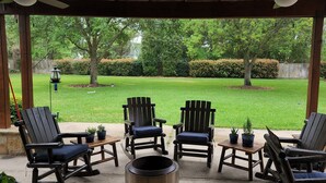 A covered patio with Adirondack chairs and a table, overlooking a well-maintained lawn and trees. - Luxury 4BR Cypress Home + Office Theater + Huge Fenced Yard + Pet Friendly (Cypress)