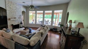 A living room with a fireplace, a sofa, a TV, and a view of the outdoors. - Luxury 4BR Cypress Home + Office Theater + Huge Fenced Yard + Pet Friendly (Cypress)