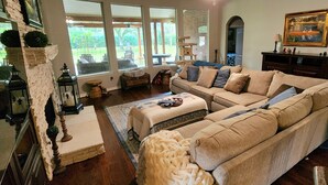 A cozy living room with a beige sectional sofa, a coffee table, and a fireplace. - Luxury 4BR Cypress Home + Office Theater + Huge Fenced Yard + Pet Friendly (Cypress)